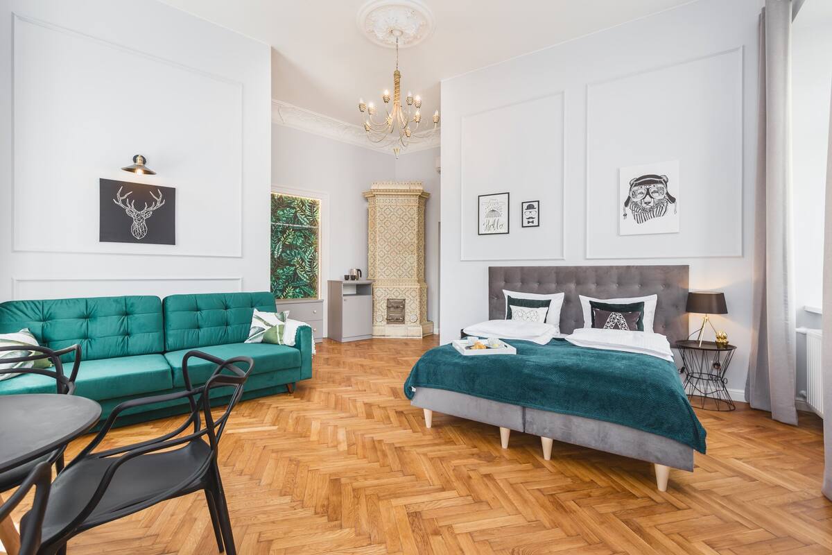 A modern bedroom with a large bed, a green sofa, a dining table, and a chandelier.