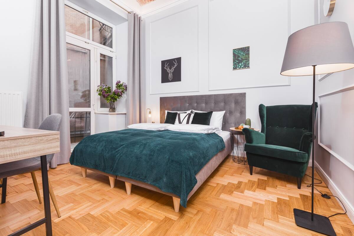 A neatly arranged bedroom with a bed, a desk, a chair, a lamp, and a window with curtains.