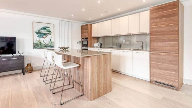 Een moderne keuken met witte kasten, een houten eiland en een eetgedeelte met barstoelen.