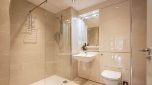 Een moderne badkamer met een douchecabine van glas, een witte wastafel en een toilet.