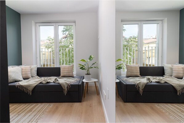 A modern living room with a black sofa, a small round table with a plant, and a view of a balcony with greenery. - Smart Apartments- Old Town Train Station (Kraków)