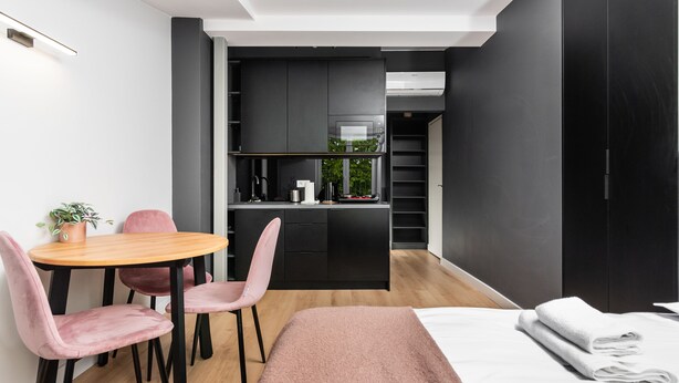 A modern bedroom with a bed, a small dining table with chairs, and a kitchenette in the background. - Smart Apartments- Old Town Train Station (Kraków)