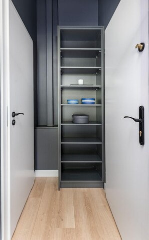 A modern storage unit with multiple shelves, a door with a handle, and a light-colored floor. - Smart Apartments- Old Town Train Station (Kraków)
