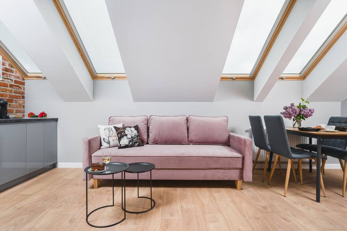 Un moderno apartamento tipo loft con un sofá rosa, un comedor con mesa y sillas, y tragaluces.