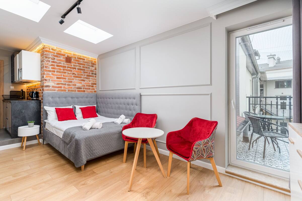 Un dormitorio moderno con cama gris, sillas rojas y vistas al balcón.