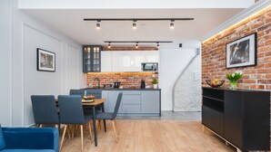 Une cuisine moderne avec un mur de fond en briques, un coin repas avec des chaises bleues et un meuble de rangement noir pour les appareils électroniques.