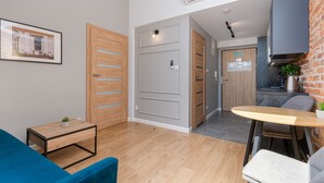 Un salon moderne avec un canapé bleu, une table basse en bois et un coin cuisine doté d’un mur en briques et d’un pot suspendu.