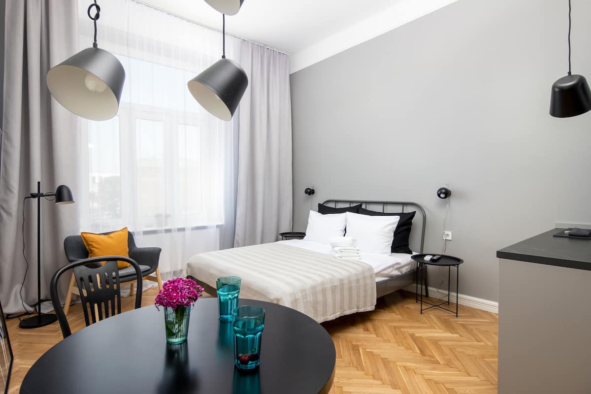 Un dormitorio moderno con una cama, mesitas de noche, un escritorio, una silla y una mesa con un jarrón de flores.