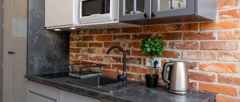 Une cuisine avec un mur en briques, un four à micro-ondes, un évier et une bouilloire.