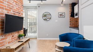 Un salon moderne avec un mur en briques, un téléviseur fixé au mur, une étagère ronde ornée de plantes, un fauteuil bleu et une petite table en bois.