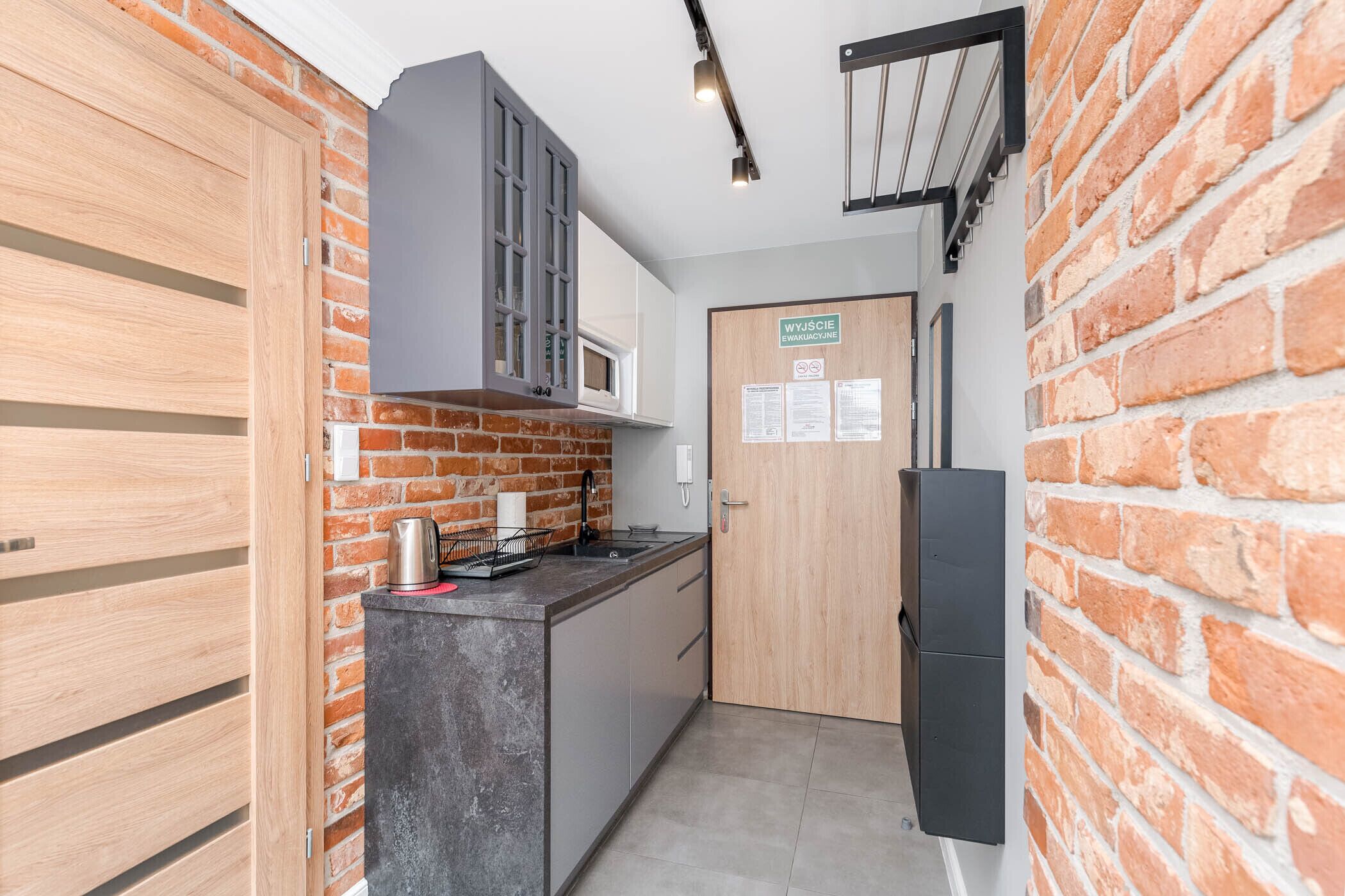 Una cocina compacta con pared de ladrillo, microondas, fregadero y puerta de madera.