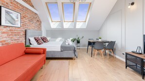 Une chambre de style loft moderne avec un plafond en pente, des fenêtres de toit, un canapé rouge, un lit gris et un coin repas avec des chaises et une table.