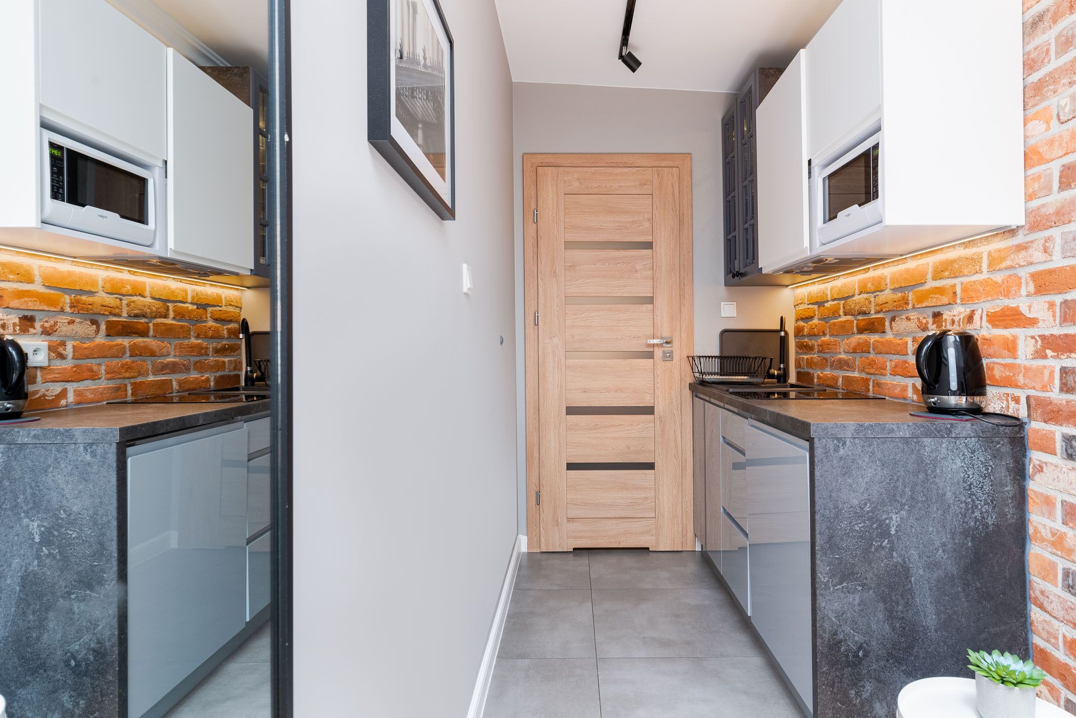 A narrow kitchen with a brick wall, a wooden door, and modern appliances.