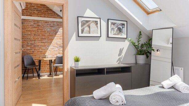 Une chambre moderne avec une lucarne, un lit agrémenté de serviettes roulées, une petite table avec des chaises, une plante en pot et des tableaux encadrés accrochés au mur.
