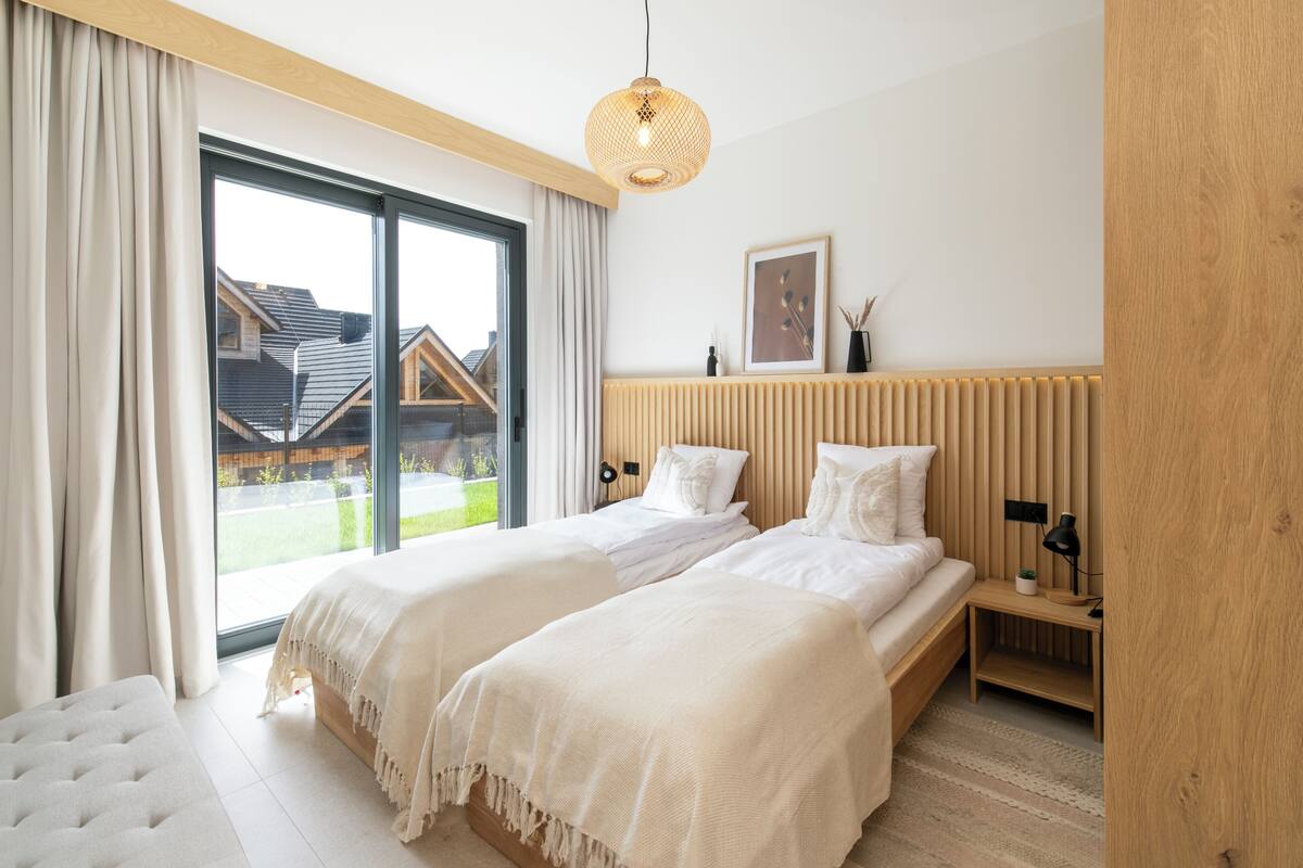 Une chambre moderne avec deux lits, une grande fenêtre et une vue sur une maison.