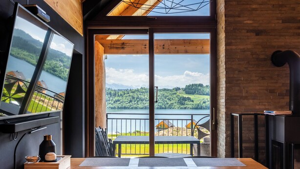 Un coin repas avec une table et des chaises, une vue sur un lac et un balcon doté d’une balustrade.