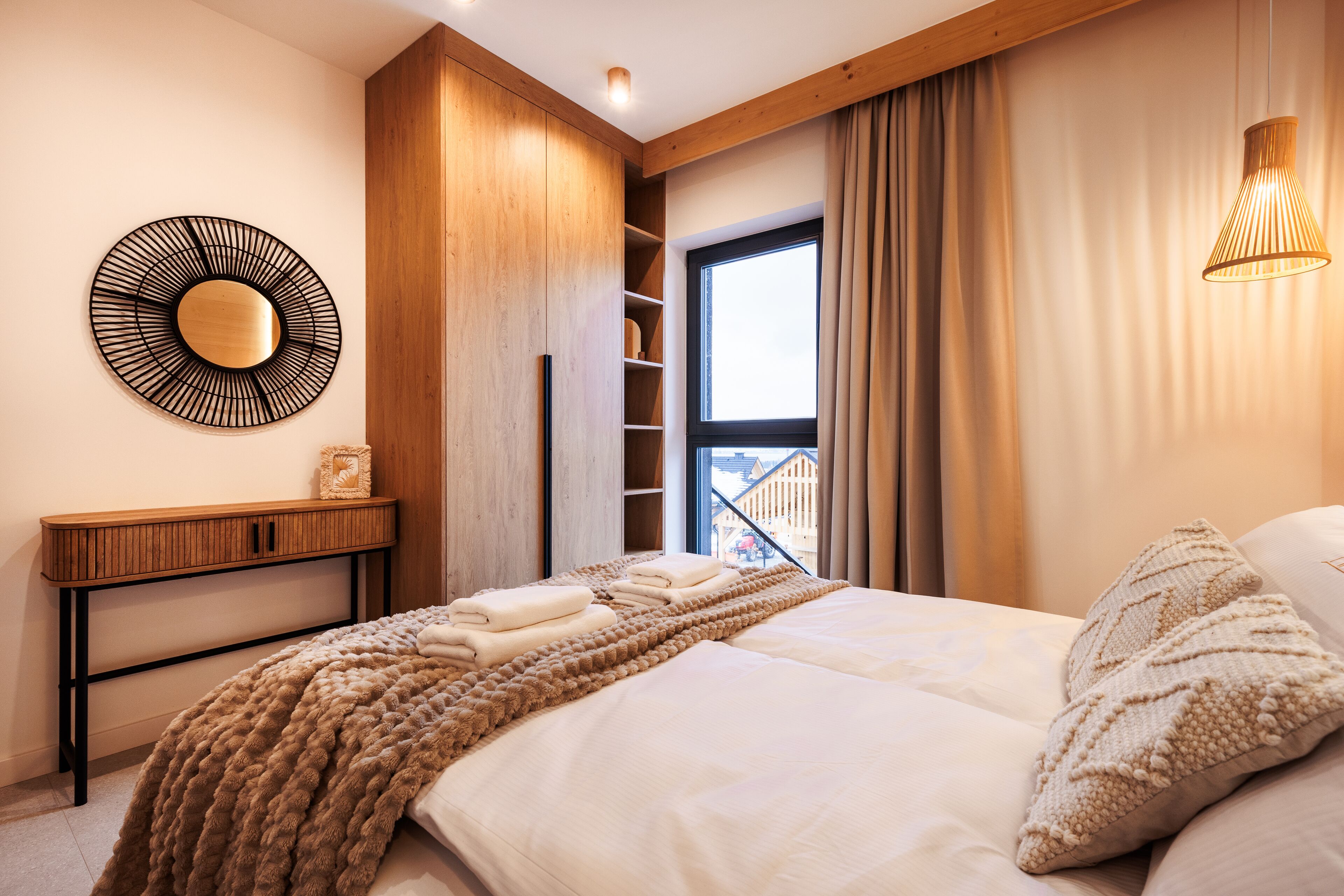 Une chambre moderne avec un grand lit, une console en bois, un miroir fixé au mur et une fenêtre avec des rideaux.