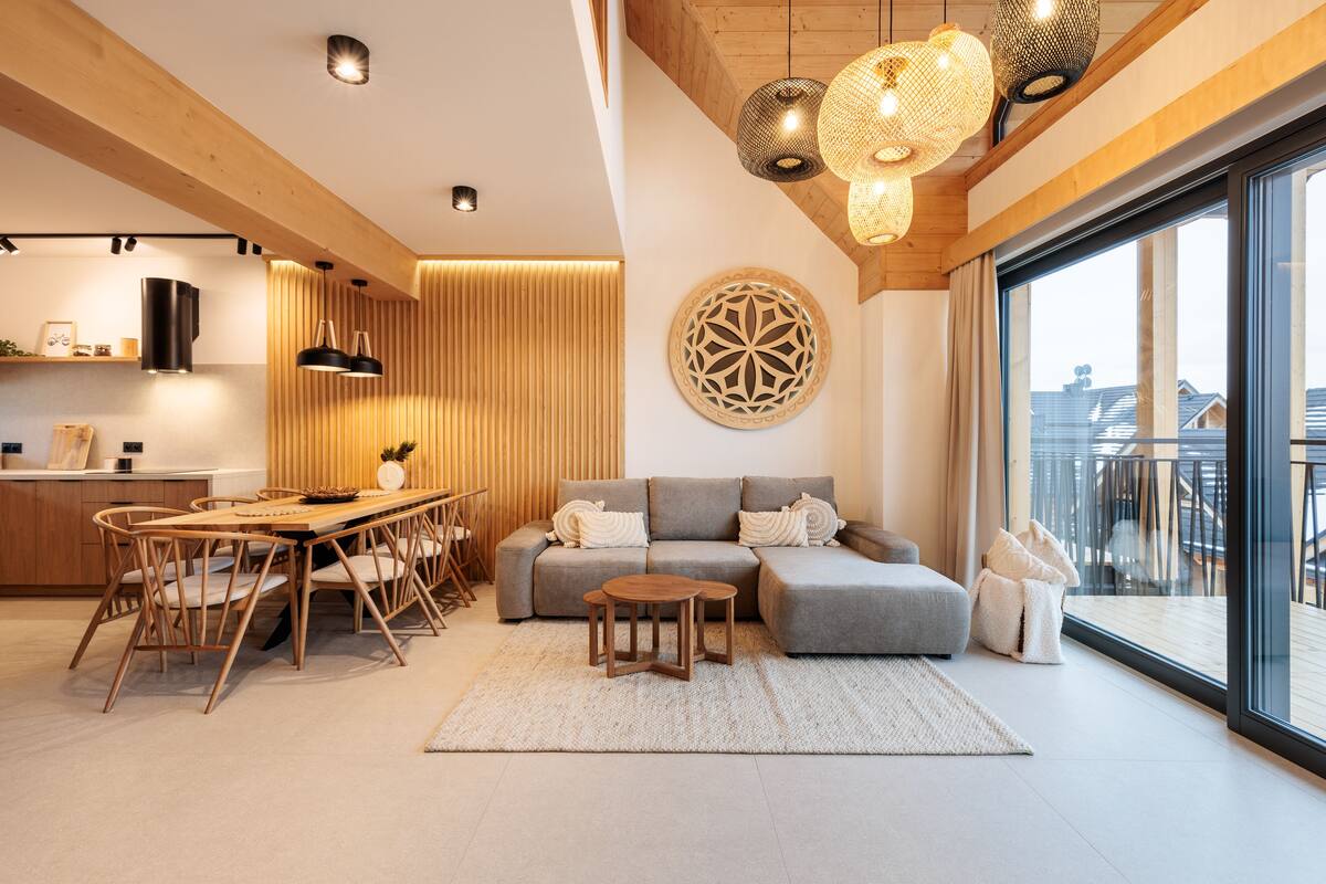 Un salon moderne avec un canapé gris, une table à manger en bois et des chaises. Une grande fenêtre offre une vue sur les bâtiments environnants.