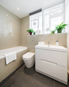 A modern bathroom with a bathtub, toilet, and vanity. - 2 bedroom apartment in Bayswater - Great views, 5 mins to Notting Hill and parks (Paddington)