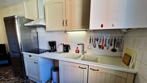 Una cocina con armarios blancos, un refrigerador de acero inoxidable, una cafetera y varios utensilios colgados en la pared.