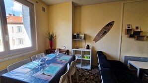 Un espacio habitable compacto con comedor, kitchenette, sofá y decoración con una tabla de surf.