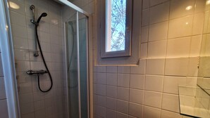 Un baño con ducha, lavamanos y ventana con vistas a árboles.