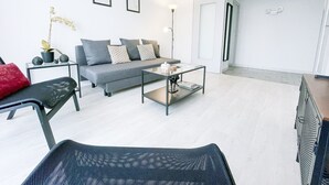 A modern living room with a grey sofa, black chairs, a glass coffee table, and a potted plant.