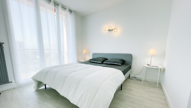 A modern bedroom with a large bed, two bedside tables, and a wall-mounted light fixture.