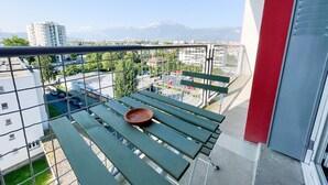 A balcony with a view of a cityscape, a metal railing, and a green bench.