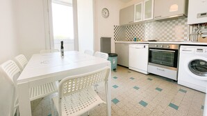 A compact kitchen with a dining table, chairs, a clock, and modern appliances including a dishwasher and oven.