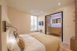 A bedroom with a bed, a TV, a bathroom with a mirror, and a window.