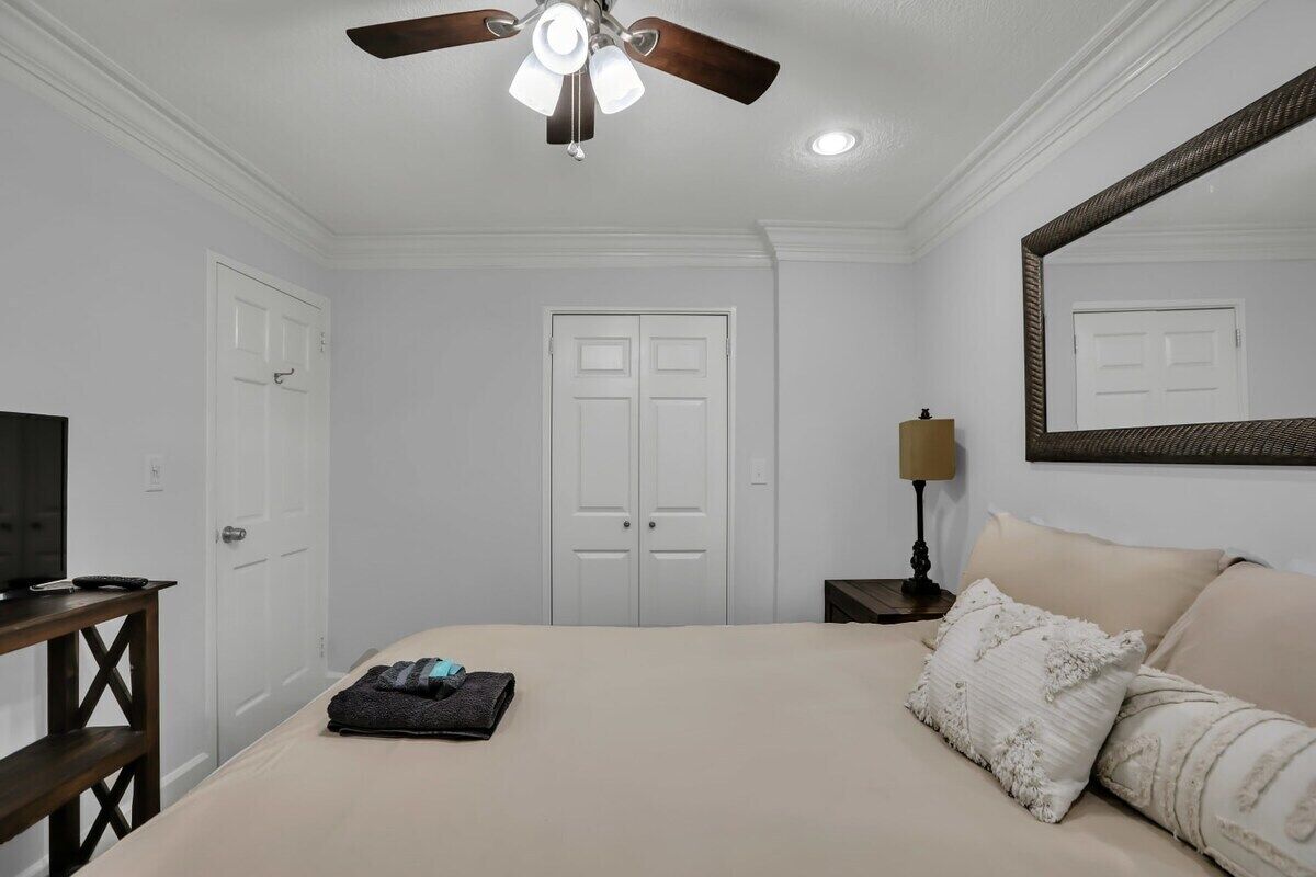 A bedroom with a bed, a ceiling fan, a television, a dresser, and a mirror.
