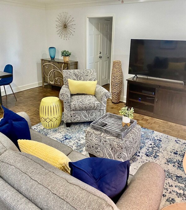 A living room with a sofa, armchair, ottoman, and a television. - FIFA 2026 Walk to Stadium | 2BR Unit 7I ATL (Atlanta)