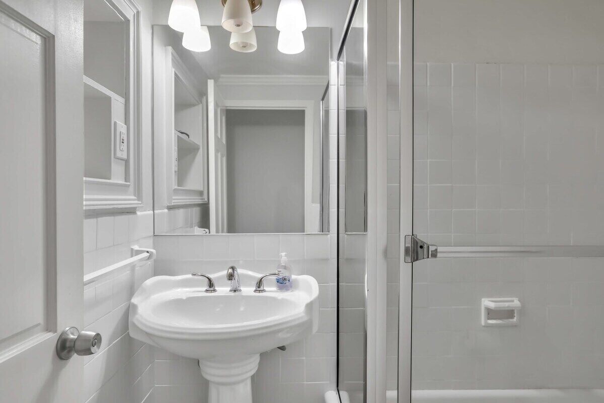 A bathroom with a pedestal sink, a mirror, and a shower enclosure.