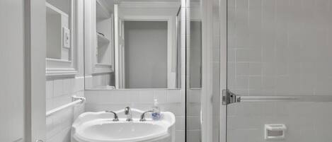Un baño con lavamanos pedestal, espejo y cabina de ducha.
