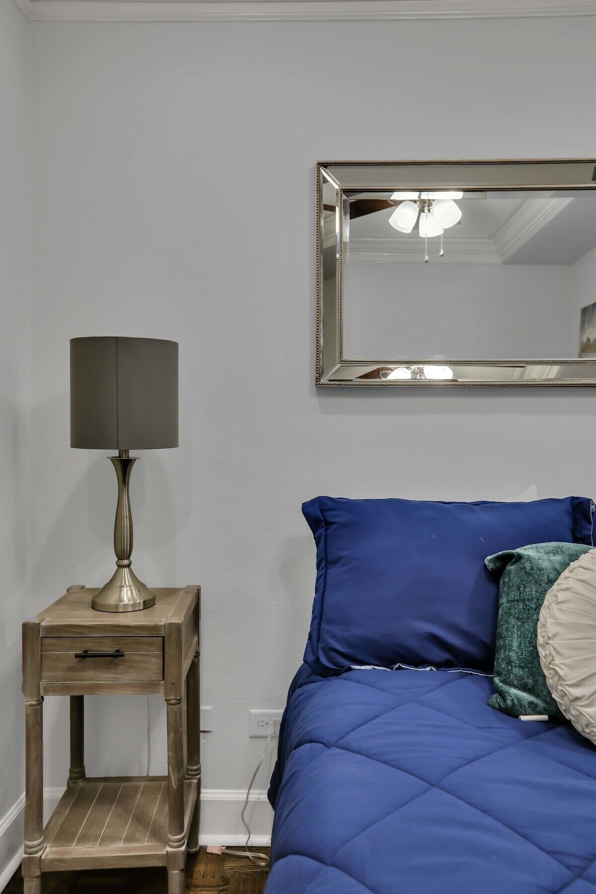 Un dormitorio con una cama, una mesita de noche con lámpara, un espejo y un mueble auxiliar.