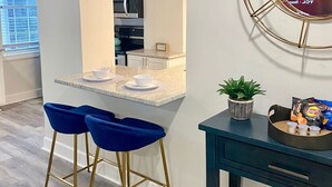 A modern kitchen with white cabinets, a granite countertop, and a built-in oven. There are two blue bar stools and a small potted plant on the counter. - FIFA 2026 Walk to Stadium | 1BR Unit 8K ATL (Atlanta)