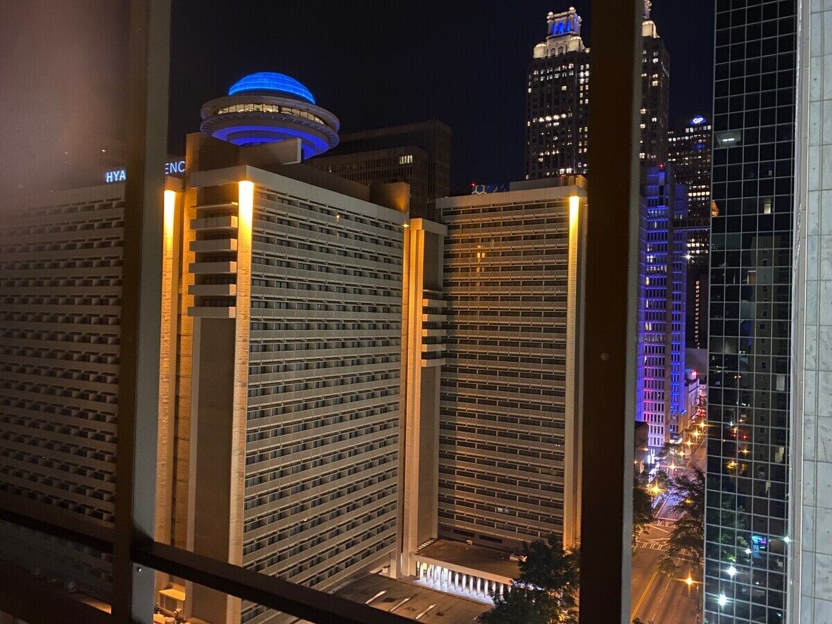 Une vue nocturne d’une ville avec de hauts immeubles, dont un hôtel doté d’un dôme illuminé d’une lumière bleue caractéristique et un bâtiment moderne en verre.