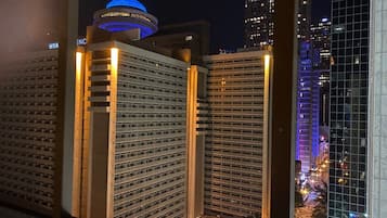Une vue nocturne d’une ville avec de hauts immeubles, dont un hôtel doté d’un dôme illuminé d’une lumière bleue caractéristique et un bâtiment moderne en verre.