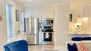 A modern kitchen with stainless steel appliances, a white dining area with a sofa and cushions, and a blue armchair. - FIFA 2026 Walk to Stadium | 1BR Unit 8K ATL (Atlanta)