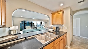 A modern kitchen with a large island, wooden cabinets, and a view into the living area.