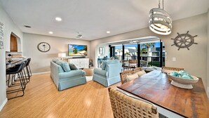 A spacious living area with a wooden dining table, light blue sofas, and a large TV screen.