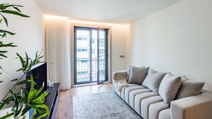 Un soggiorno moderno con un divano, una TV, una pianta e una porta scorrevole in vetro che dà su un balcone.