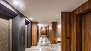 Un corridoio moderno con pavimento in marmo, rivestimento in legno e diverse porte che conducono a delle stanze.