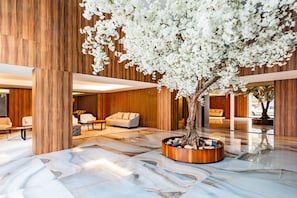 A modern lobby with a large tree, wooden paneling, and a marble floor. - Renovato Prestige (Porto)