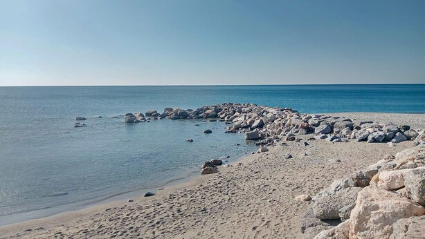 Une plage rocheuse bordée d’une eau d’un bleu limpide et d’une étendue de sable.
