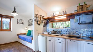 Une cuisine de taille réduite avec des meubles blancs, un plan de travail en bois et une fenêtre au-dessus de l’évier.
