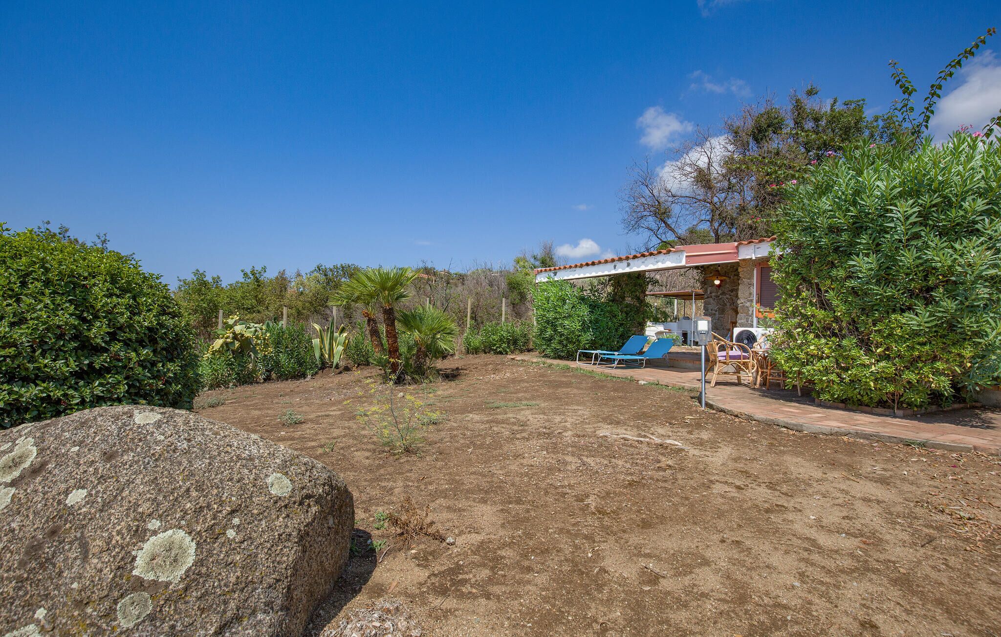 A covered outdoor area with a stone wall, a large rock, and a patio with a table and chairs.