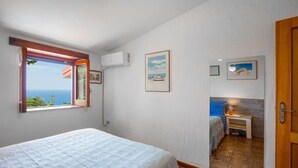 Une chambre à coucher avec un lit, une fenêtre donnant sur la mer, une salle de bain avec un miroir et une porte.