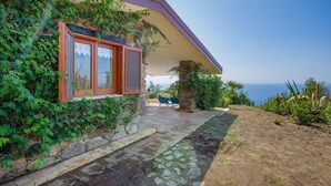 Une maison avec un chemin de pierre menant à un patio couvert où se trouvent deux chaises, le tout donnant sur une étendue d’eau.